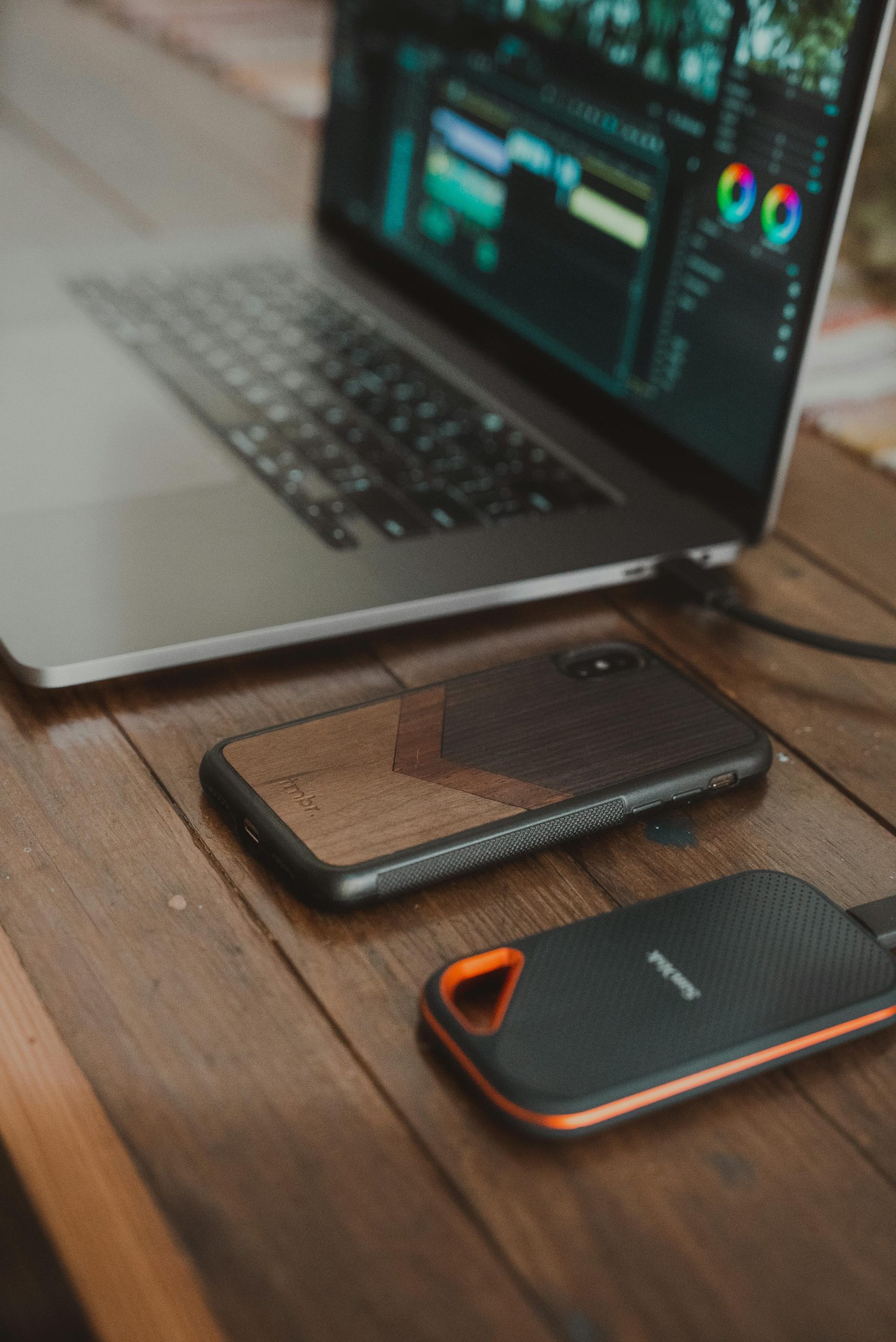 A minimalist workspace featuring a laptop, smartphone, and portable drive on a wooden table.